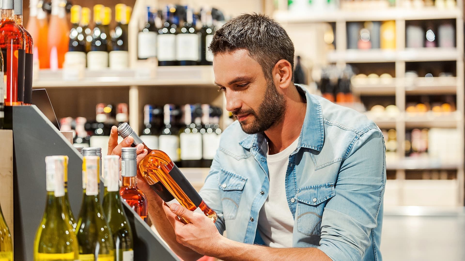 Mann begutachtet eine Weinflasche in einem Getränkemarkt